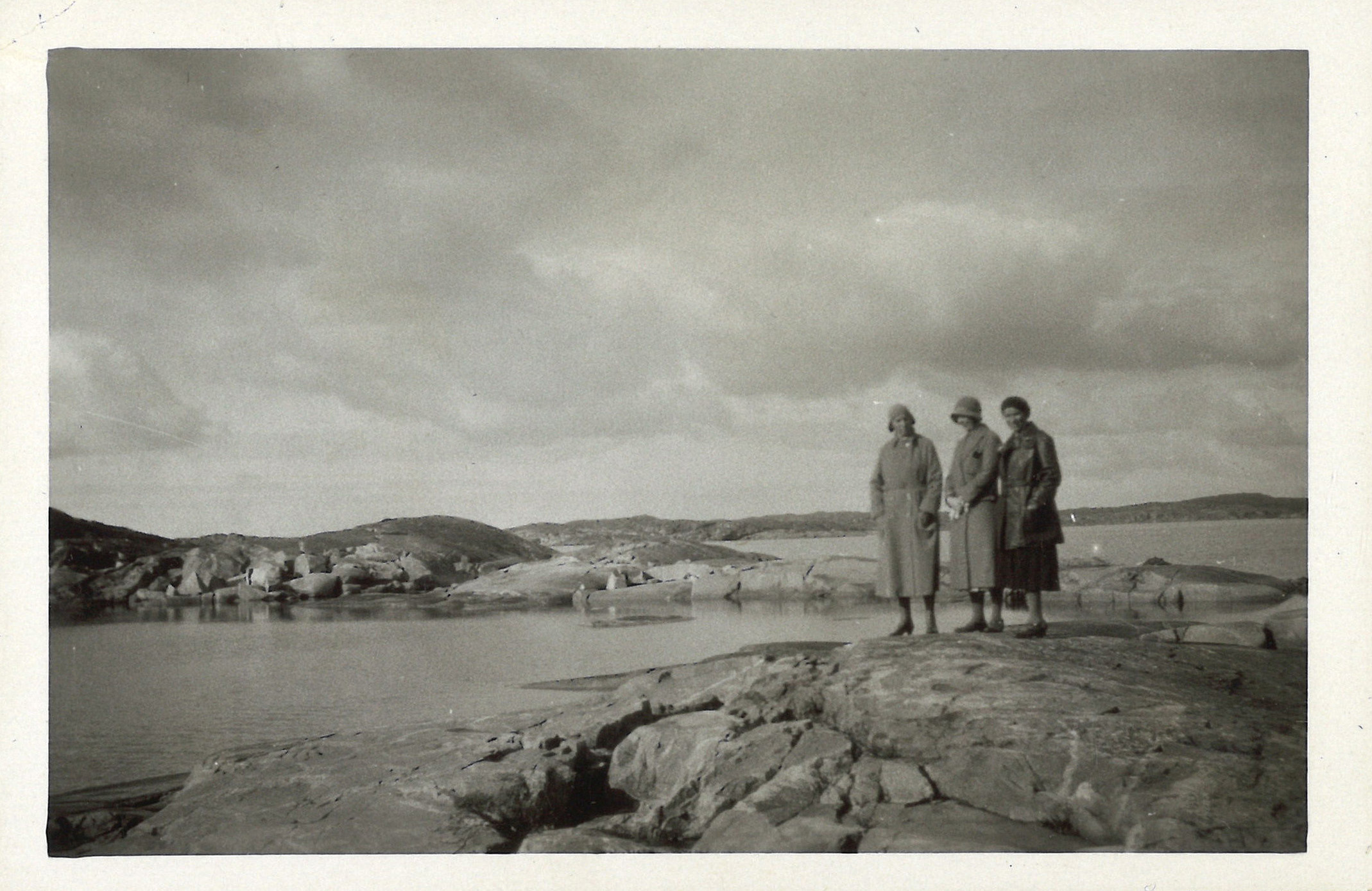 
                    Ett svartvitt fotografi av tre kvinnor som står på en klippa i Göteborgs skärgård. 
                    