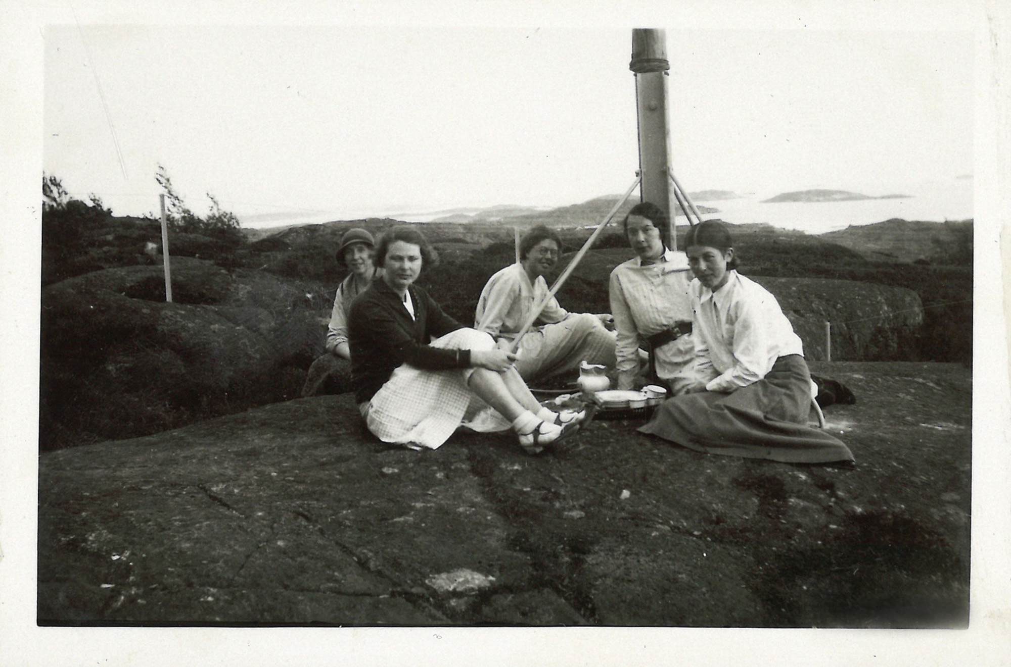 
                    Ett svartvitt fotografi av fem kvinnor sitter på en klippa i Göteborgs skärgård. Mellan sig har de en bricka med karaff och koppar. 
                    